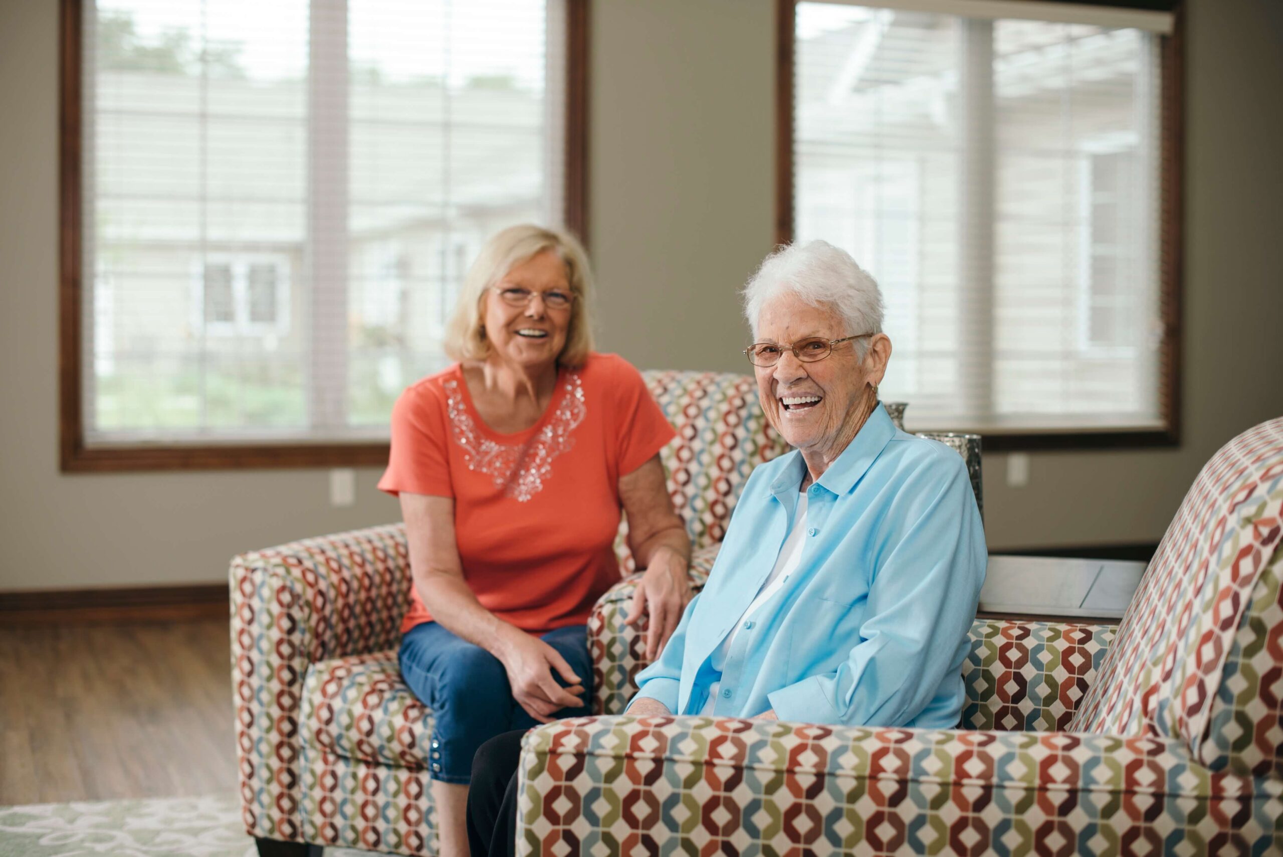 Two seniors smiling and sitting in the living room of a senior living community