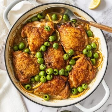Round dish with the Braised Chicken,, Lemon and Olives, with a spoon resting in the dish.