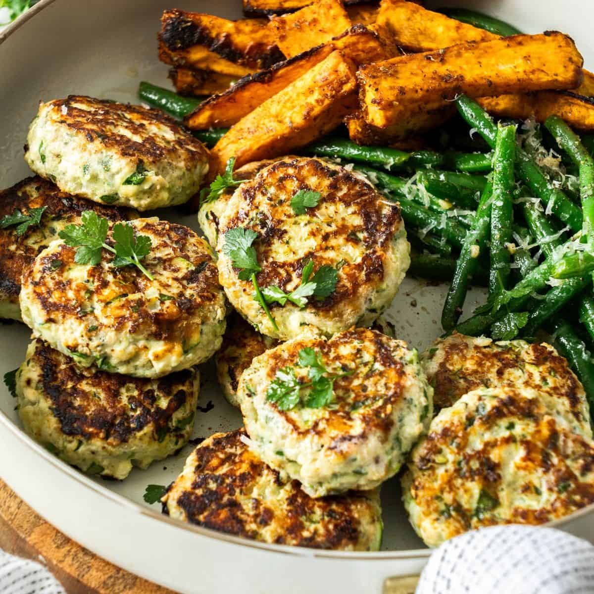 Round dish of Chicken Rissoles, with some green beans and sweet potato wedges on the side.