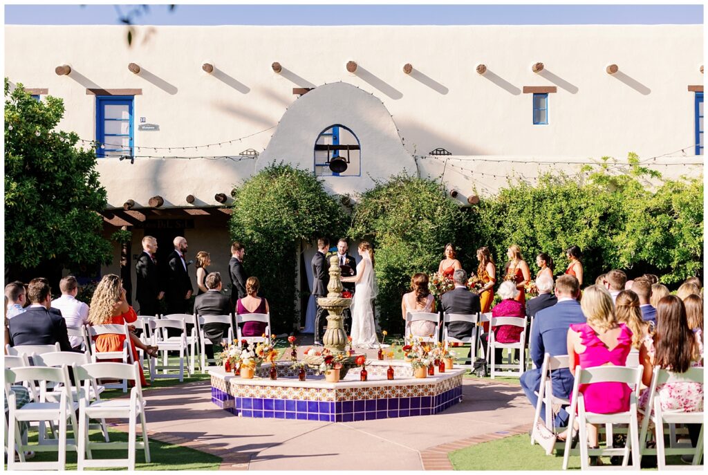 Bride and groom hold hands during their wedding ceremony at Hacienda Del Sol Wedding Venue in Tucson, Arizona. Family and friends watch them exchange their vows.