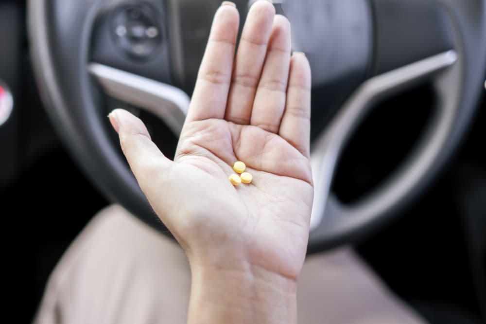 Taking medication before driving with the woman hand holding allergies pills behind the steering wheel