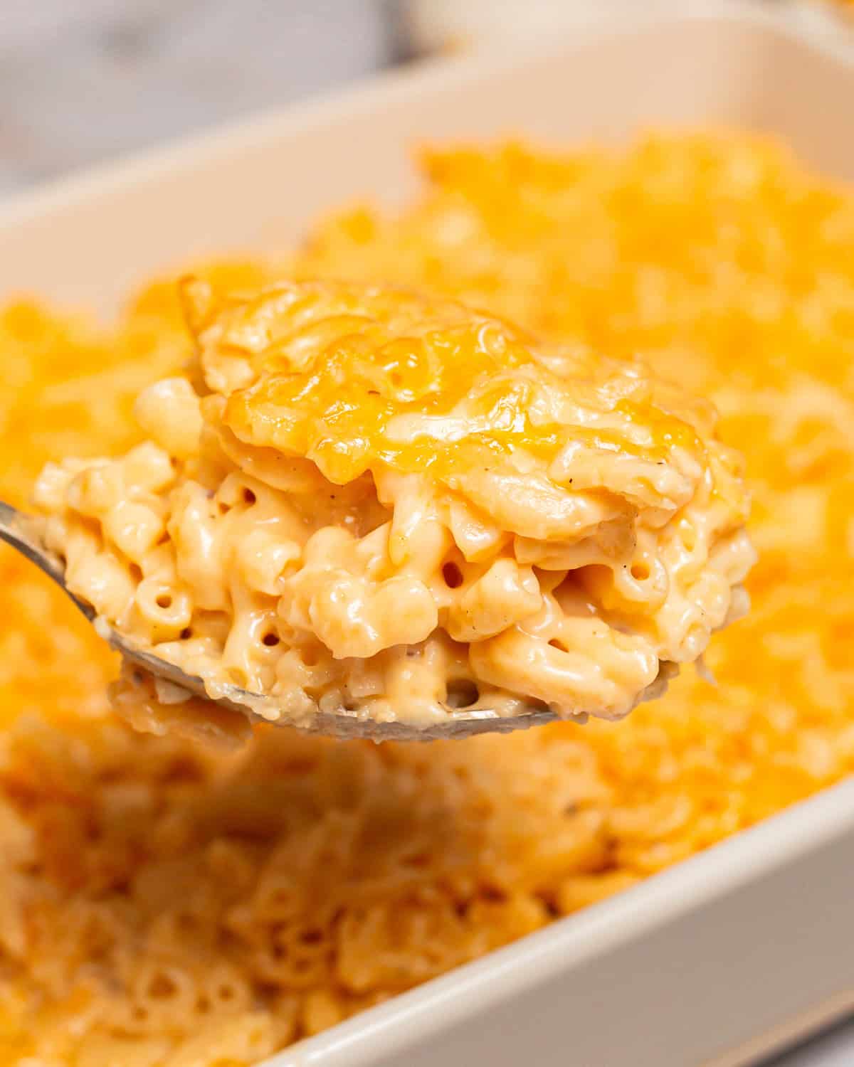 a spoon holding a scoop of chick fil a mac and cheese above a casserole dish.