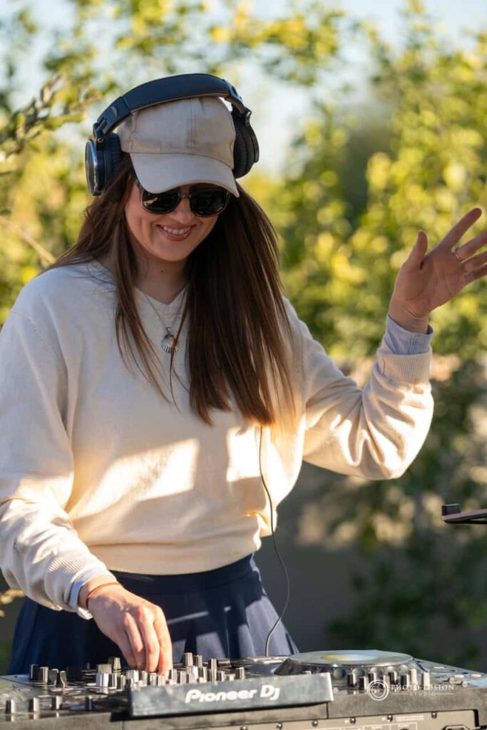 Event Photography for an Unforgettable First Birthday 40 DJ at a one year olds birthday party. She has her headphones on and one hand in the air with theother turning the dials on the DJ board. She has a smile on her face as she works.