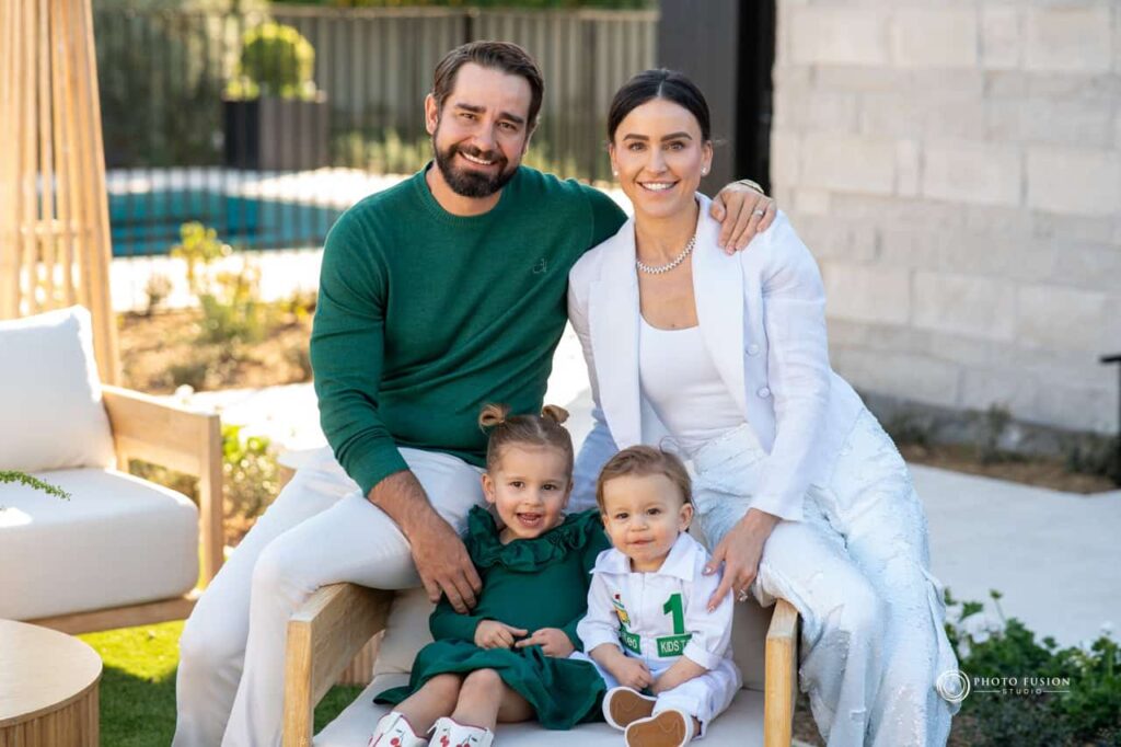 Event Photography for an Unforgettable First Birthday 46 family photo of the two parents and two kids. The little boy on the bottom right is turing one. The family is smiling and looking at the camera as they are celebrating their one year olds birthday.