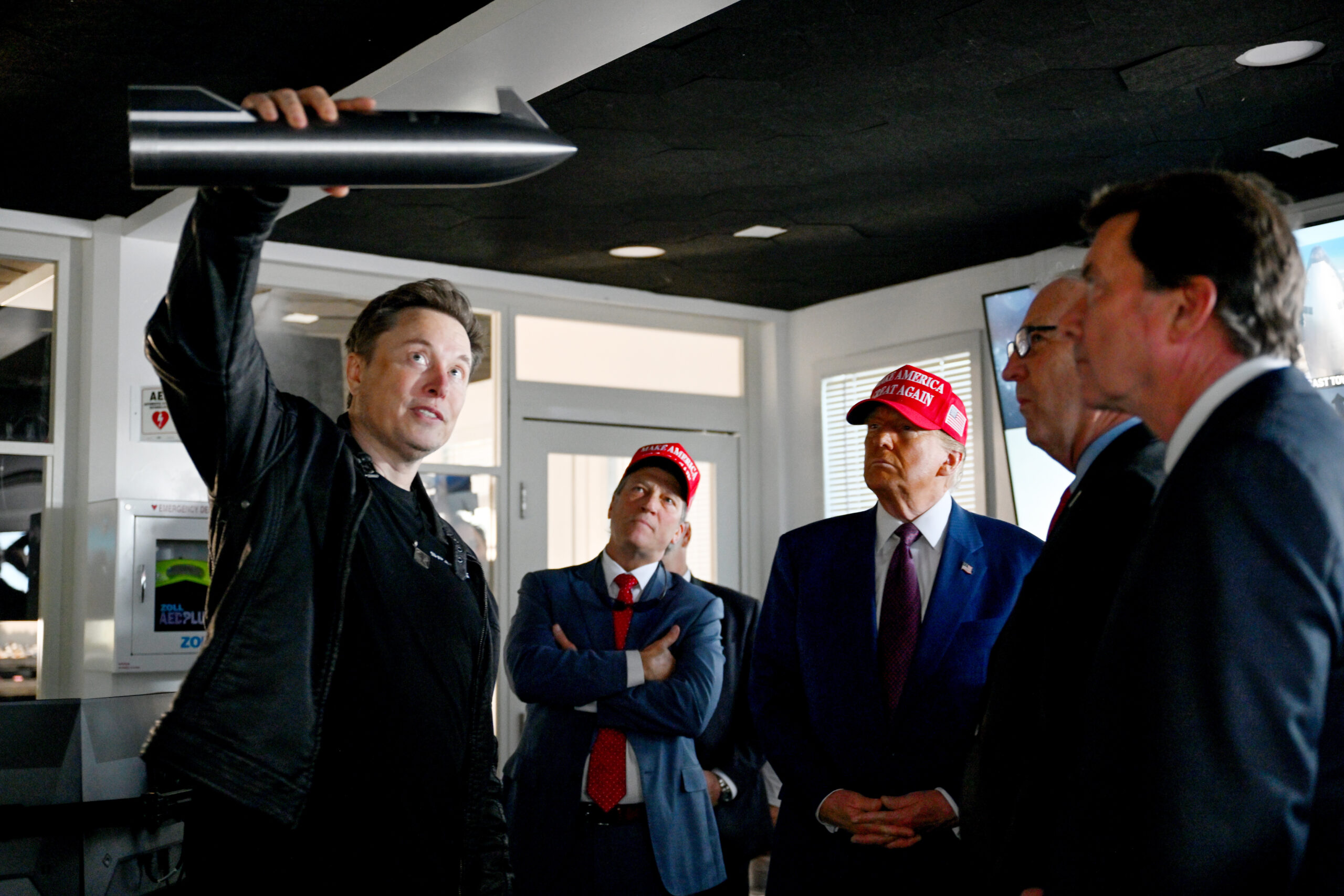 Musk holds a model rocket over his head while speaking with Trump and others.
