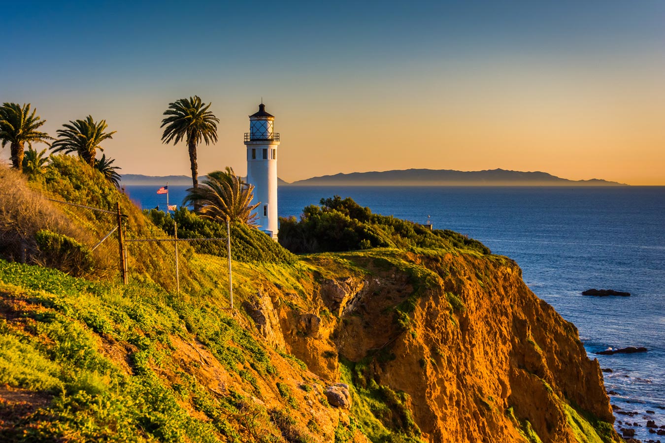 a lighthouse on top of the hill during the sunset near the ocean