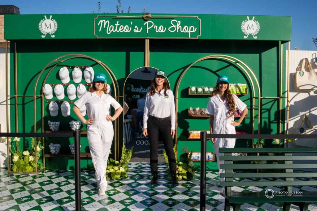 Event Photography for an Unforgettable First Birthday 43 There are three ladies who are posted in mateos pro shop smiling at the camera. The lady in the ccenter has on black pants, a custom white polo, and a green hat that says caddie on it. Both the ladies on the side are wearing white caddie uniforms and have green hats on that say caddie on them as well.
