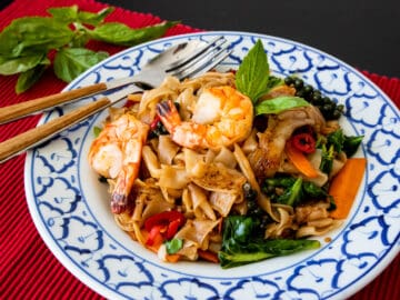 A plate of drunken noodles with shrimp on red placemat