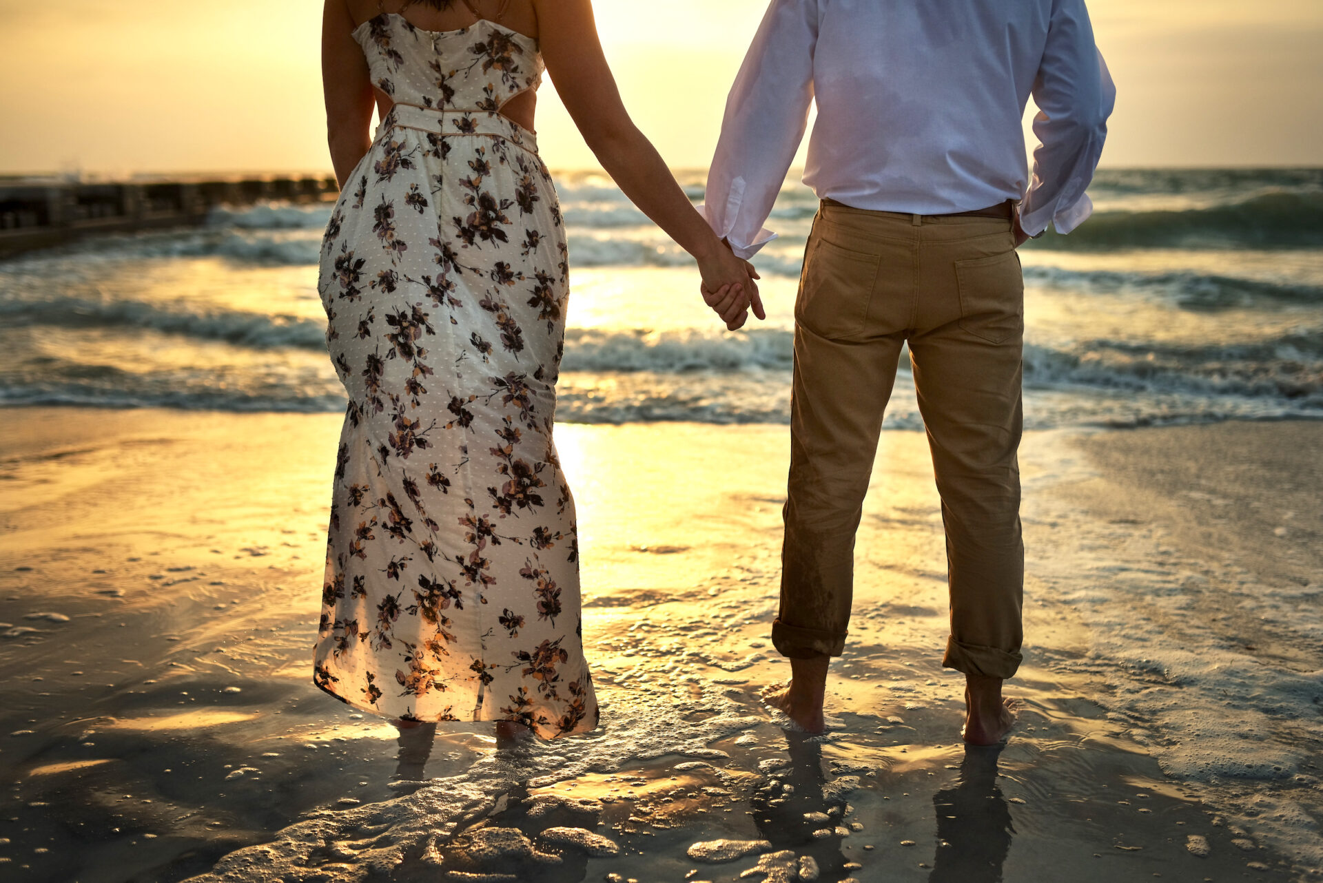 Rearview shot of an unrecognizable couple holding hands while standing on the beach.