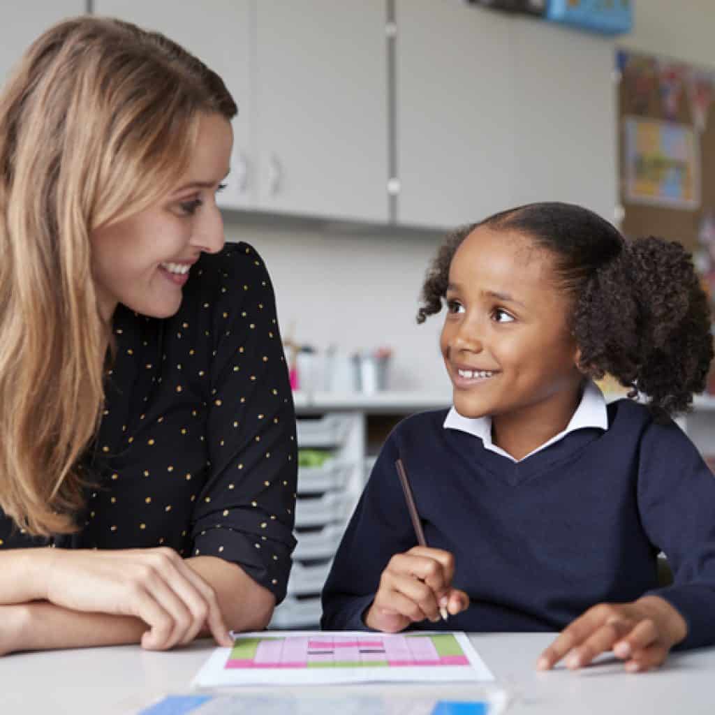 Teaching Assistant working 1:1 with school girl smiling at each other - using AI in Education to increase teacher student face-to-face time