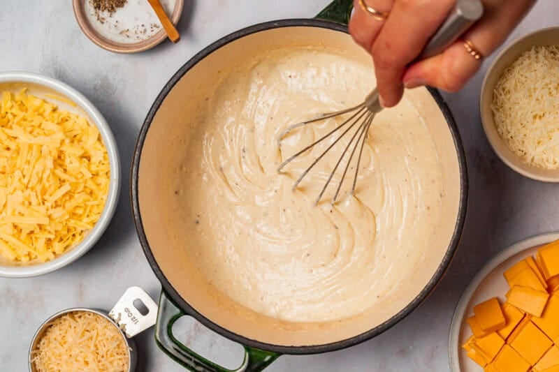 whisking milk into a roux in a dutch oven with a whisk.