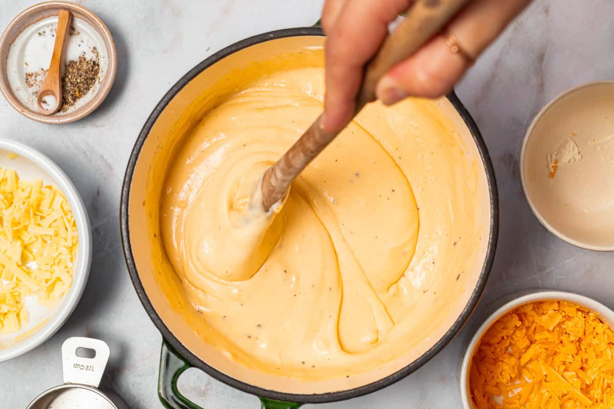 stirring creamy cheese sauce with a wooden spoon in a dutch oven.